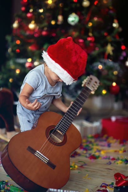 istock Boy is playing in front of a decorated Christmas tree with guitar 1192095815