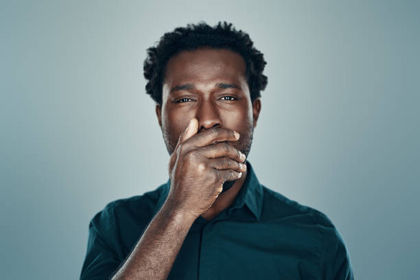 istock Handsome young African man looking at camera and covering mouth with hand while standing against grey background 1192095882