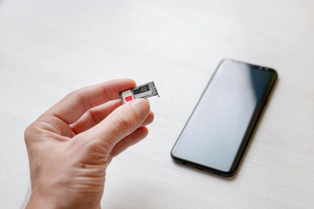 istock SIM card tray holder micro SD card slot adapter in hand. Smart phone in background 1192102425