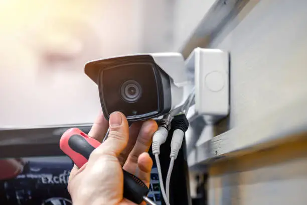 Photo of Close-up of surveillance camera installation, male hand holds cctv camera