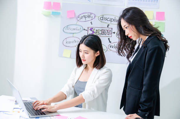 istock Two asian hardworking young female entrepreneurs working together on a laptop computer reading the screen with serious engrossed expressions, Agile scrum concept 1192103889