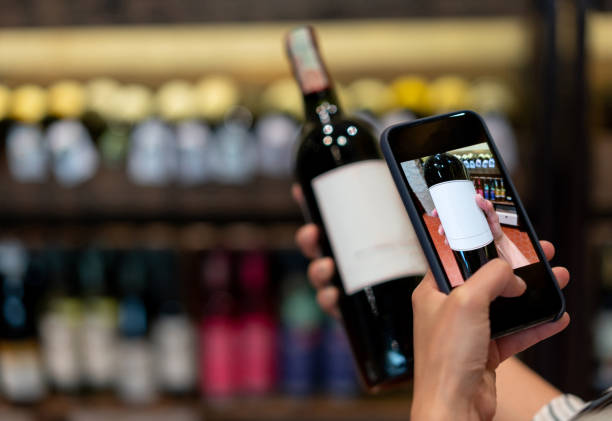 клиент в подвале сканирует бутылку вина с помощью мобильного телефона - wine rack фотографии стоковые фото и изображения