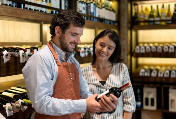 istock Sommelier talking to a woman at a wine bar while holding a bottle 1192104498