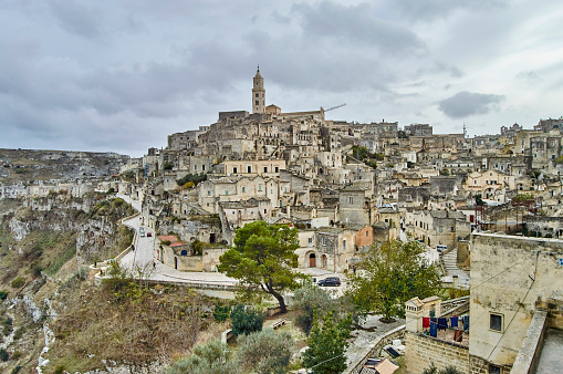 Tourists visiting the ancient historic Italian city Sassi Di Matera that has been build into a mountain. Caves with a brick wall facade. The City is part of Unesco World Heritage project.