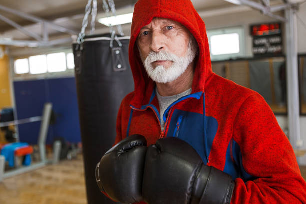 Senior man training boxing in gym looking at camera Senior man training boxing in gym old man boxing stock pictures, royalty-free photos & images