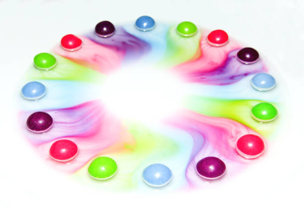 A variety of vibrant candies in different colors spill out of a vintage tin container, creating a striking visual display against a dark background.