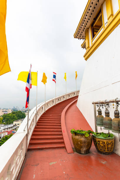 escadas à parte superior do templo de wat saket (montagem dourada) na cidade de banguecoque, tailândia. bandeira de tailândia e bandeira do budismo perto das escadas vermelhas. panela com lírio-adágua é colocada em terra. panorama de banguecoque. - monastery buddhism wat east - fotografias e filmes do acervo