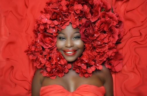 Beautiful African woman smiling wearing red flowers on hair lying on red fabric background