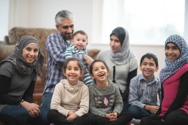 Casual Muslim Family Portrait stock photo A large Muslim family sit on the floor of their living room posing for a casual family photo.  The older girls are each wearing a Hijab and everyone is dressed casually. 6 11 months stock pictures, royalty-free photos & images