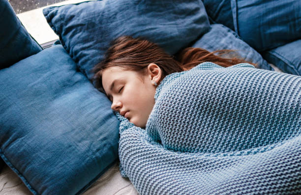 Young teenager girl sleeping snuggled in warm knitted blue blanket. Seasonal melancholy, apathy and winter blues. Cozy home. stock photo