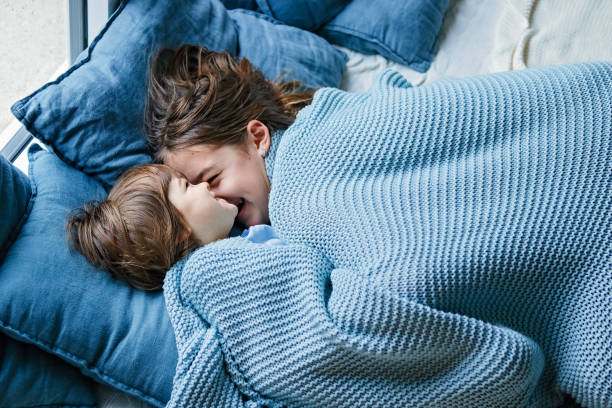 Happy siblings snuggling under warm knitted blanket. Little boy and his teenager sister enjoying staying at home at cold winter day having fun together, Family quality time on holidays. Happy siblings snuggling under warm knitted blanket. Little boy and his teenager sister enjoying staying at home at cold winter day having fun together, Family quality time on holidays. blue interiors stock pictures, royalty-free photos & images