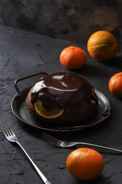 Homemade winter dessert. Sweet chcocolate pudding with oranges and tangerines on black background copy space. Low key still life high angle view