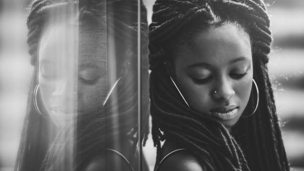 Portrait of a charming African girl Portrait of a charming African girl with long braids leaning against the mirror which fully reflects her; dazzling young Guinean woman with braided hair is leaning on a glass reflecting wall outdoors braided hair photos stock pictures, royalty-free photos & images