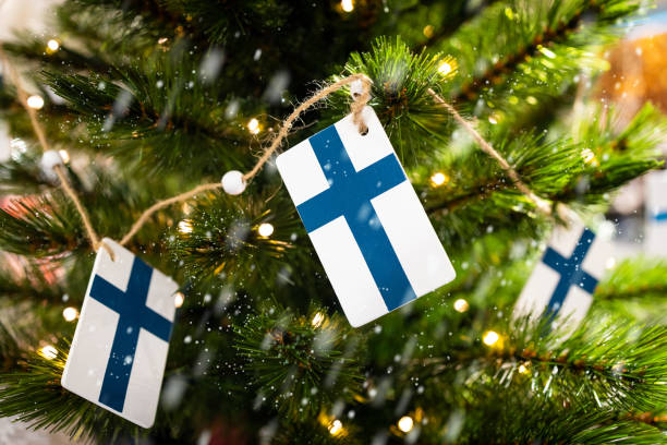 Flags of Finland on a Christmas tree with garland lights in focus. Background and snowfall blurred. stock photo