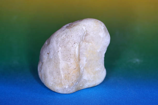 A stone with three natural perforations lies on a reddish rock, resembling a face, set against a pebble backdrop