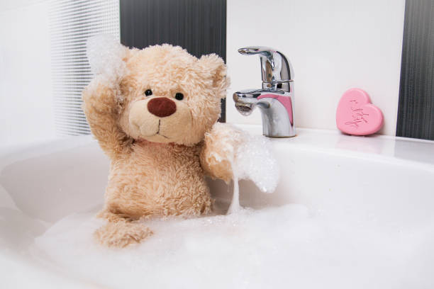 A cute teddy bear is sitting in the basin and washing.