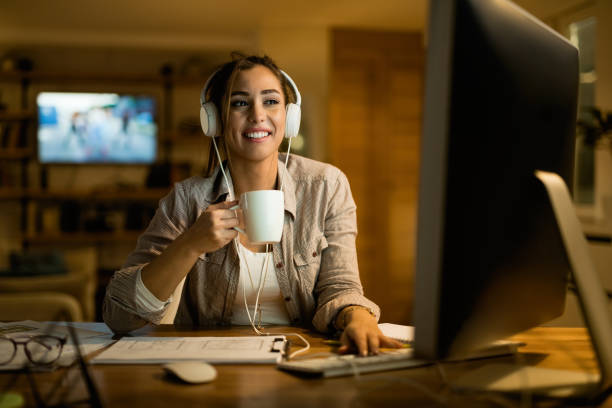 femme heureuse avec des écouteurs surfant sur le net sur le pc de bureau la nuit. - hot drink audio photos et images de collection