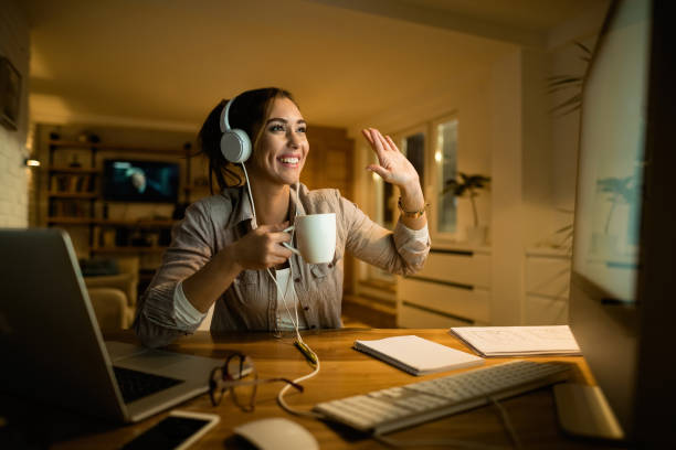 szczęśliwa kobieta ze słuchawkami wykonująca rozmowę wideo przez komputer w nocy. - non alcoholic beverage audio zdjęcia i obrazy z banku zdjęć
