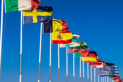 Flags of EU countries on a white flagpoles against a blue sky