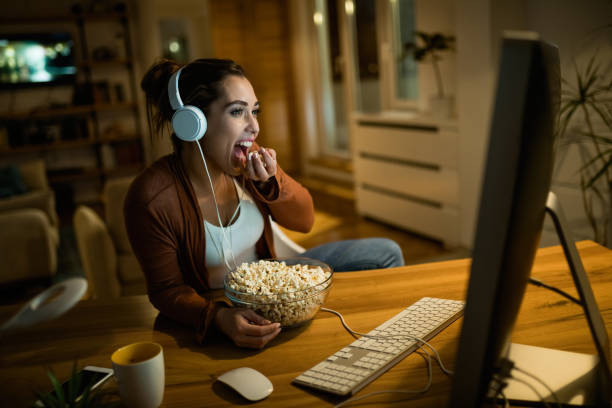 istock Young woman eating popcorn while watching movie on desktop PC at home. 1192138568