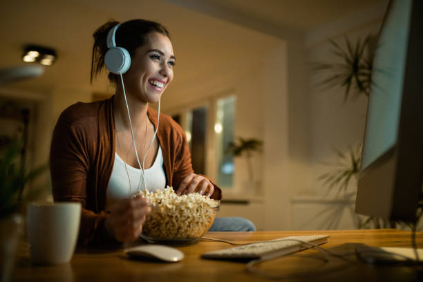 istock Happy woman surfing the net on a computer while eating popcorn at night. 1192138631