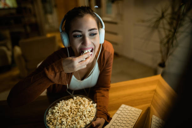 istock Young woman with headphones eating popcorn while using computer at night. 1192138738