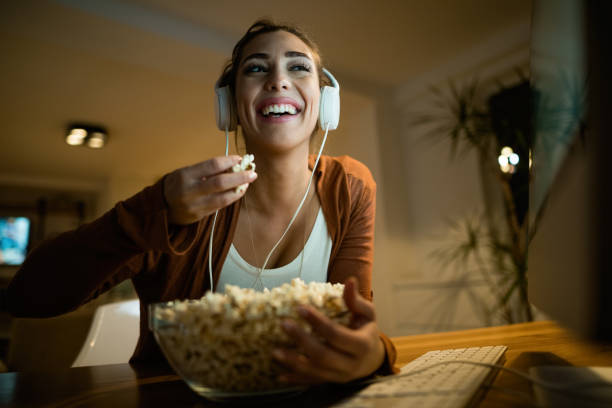 istock Below view of happy woman using computer while eating popcorn at night. 1192138893
