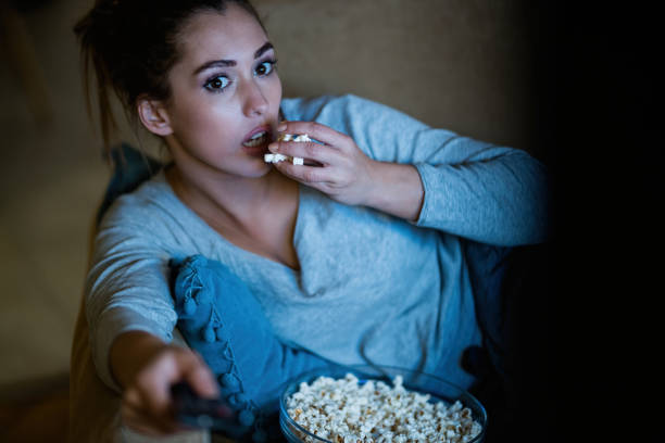 istock Young shocked woman changing channels on TV while eating popcorn at night. 1192140883