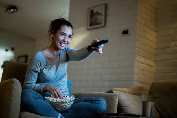 istock Happy woman using remote control while watching TV and eating popcorn at night. 1192141413
