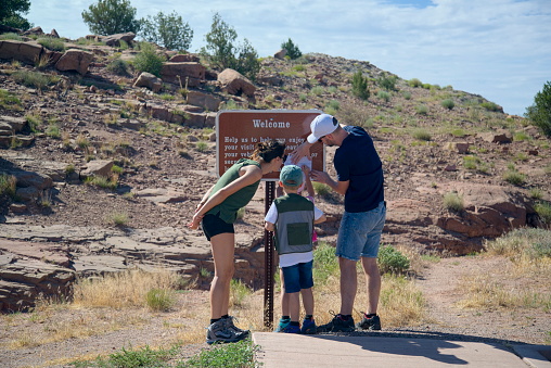 South Rim Canyon de Chelly National Park, July 7, 2019: Family of four tourist looking at an information sign at the Canyon de Chelly Tunnel Overlook along the canyon’s south rim. There are two elementary school age children, twins at that, with their parent.