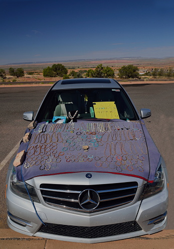 South Rim Canyon de Chelly National Park, July 7, 2019: A Navajo vendorcar displays her native American’s  craft work in the parking for the Tsegi Overlook on the hood of her Mercedes with the hood cover held on using bricks.  Business must be good for indian jewelry
