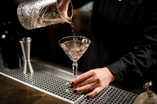 Close up of alcohol flowing from stainless steel strainer to cocktail glass