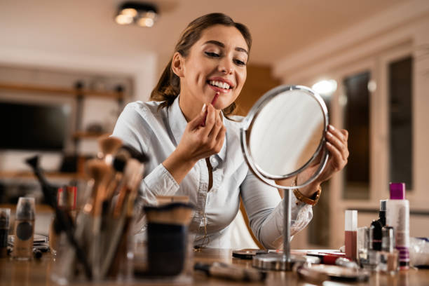 jeune femme de sourire appliquant le doublure de lèvre tout en se regardant dans un miroir. - lip liner photos photos et images de collection