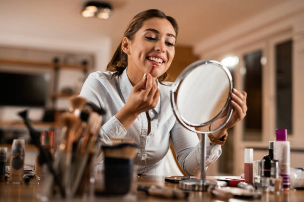 young smiling woman applying lip liner while looking herself in a mirror. - lip liner fotos imagens e fotografias de stock