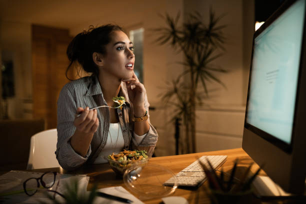 istock Young woman reading an e-mail on desktop PC while eating salad at home. 1192150027