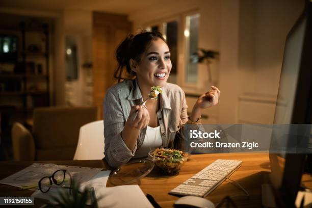 Young Woman Eating Salad While Working On A Computer Late At Night Stock Photo - Download Image Now