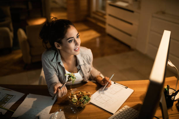 istock Above view of freelancer working on a computer and eating salad at night. 1192150301