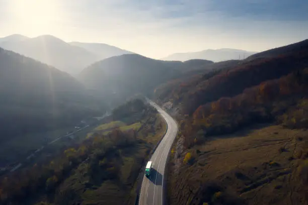 Transportation background. Truck moving on free highway in mountains at sunrise.