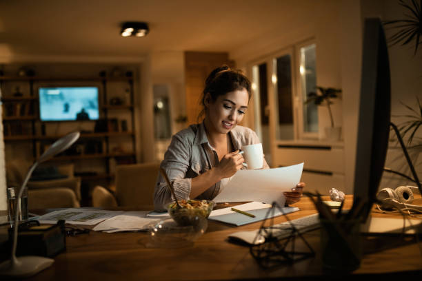 istock Smiling woman drinking tea while learning in the evening at home. 1192151143