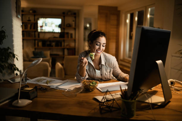 istock Happy freelance worker going through paperwork while eating salad in the evening at home. 1192151197