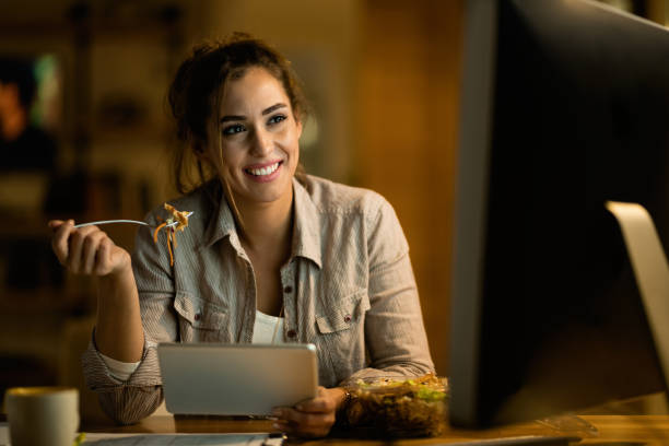 istock Smiling woman eating salad while working at night at home. 1192151783