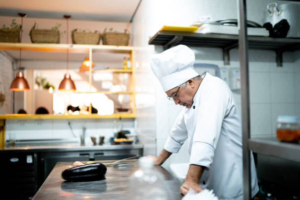 A worried senior chef in the kitchen counter A worried senior chef in the kitchen counter working seniors stock pictures, royalty-free photos & images