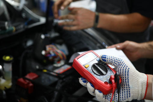 Close-up of male hands checking voltage of automobile battery under hood machine with accuracy. Automechanic using modern utility. Automotive checkup concept