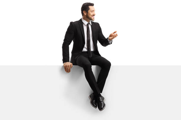 istock Handsome young man in a suit sitting on a blank panel and gesturing with hand 1192194091