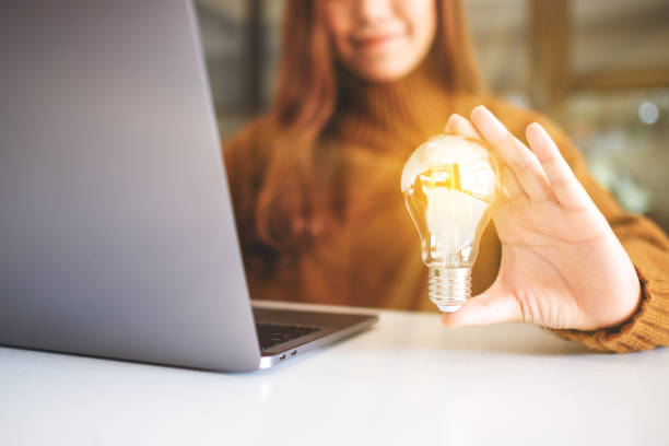 istock a businesswoman holding and showing a glowing light bulb while working on laptop 1192196289