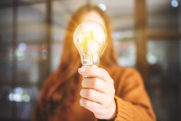 a woman holding and showing a glowing light bulb - light bulb business wisdom abstract imagens e fotografias de stock