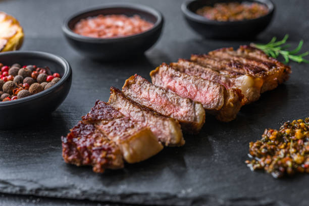 New york strip loin beef steak meat with chimichurri sauce against black stone background stock photo