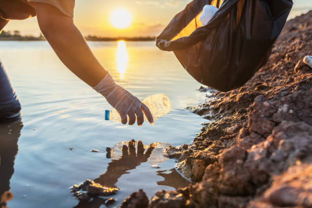 istock people volunteer keeping garbage plastic bottle into black bag on river in sunset 1192215249