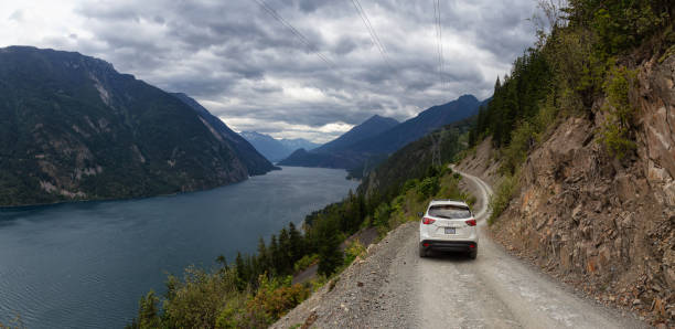 Driving in Interior BC Lillooet, BC, Canada - August 17, 2019: Mazda SUV driving on a Dirt Road in the Mountain Valley near a lake during a cloudy summer evening. pemberton bc stock pictures, royalty-free photos & images