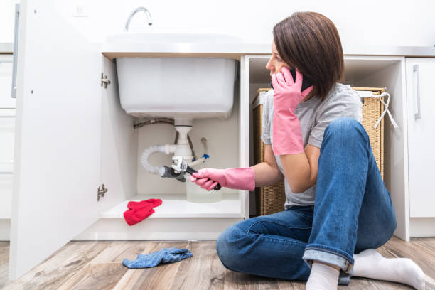 Woman sitting near leaking sink sking for help by phone Woman sitting near leaking sink calling for help Plumber stock pictures, royalty-free photos & images